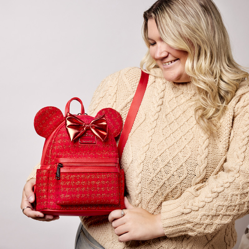 Woman wearing a beige knit sweater and holding the Minnie Mouse Red Glitter Tonal Mini Backpack 
